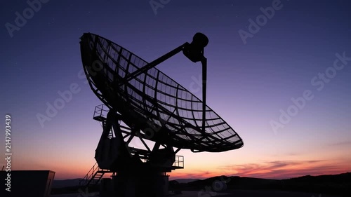 Silhouette of a large radar antenna rotating slowly under a starry twilight sky for space tracking