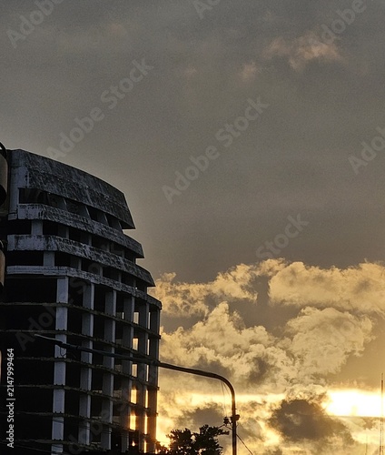 Old abandoned concrete building structure against a dramatic golden hour sunset sky with glowing clouds for urban decay concepts.