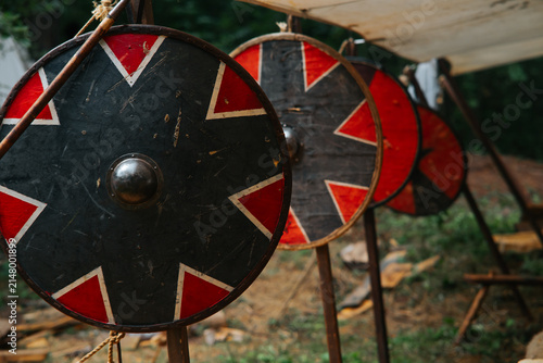 Foto Several wooden shields with red and black designs are arranged in a line under a canvas shelter