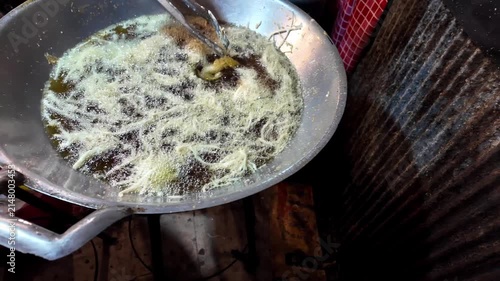 Close-up of a street food vendor pouring thin batter into boiling oil in a large wok to prepare a traditional Thai fried dessert at a night market. Authentic Asian street food cooking with bubbling oi