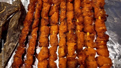 Close-up of grilled crocodile meat skewers displayed for sale at a Thai night market with a visible crocodile sign. Exotic street food in Thailand featuring roasted crocodile meat on wooden skewers. A
