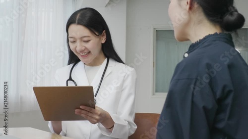 Young Japanese female doctor writing on medical chart during patient examination