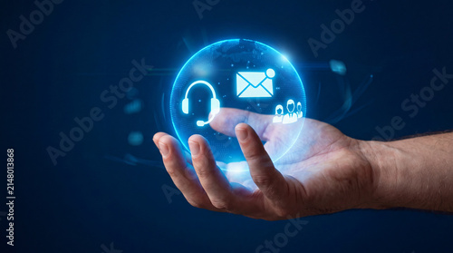 Human hand holding a glowing digital sphere featuring customer service icons including headset, email envelope, and support team members on dark blue background