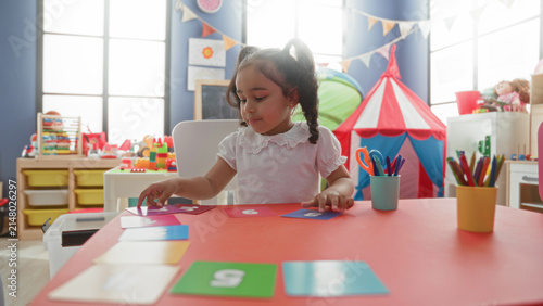 Canvas Print Girl placing number cards with hand on a red activity table, sitting in a bright playroom with tent and toy storage in building; concentration learning