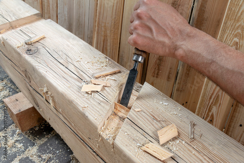 Close-up of a carpenter using a wood chisel to create a precise joint in a timber beam during woodworking and construction work. Concept of craftsmanship, woodworking, timber framing, DIY project