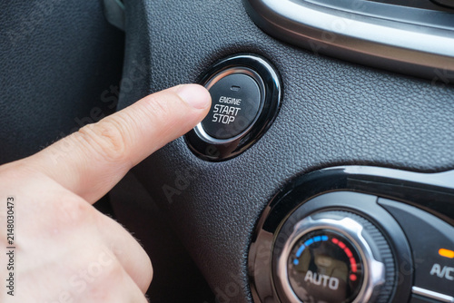 A close-up of a man's finger pressing the start button in a car.