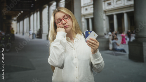 Foto Woman holding creditcard and debitcard, resting chin on fist while studying cards in building colonnade; boredom indecision