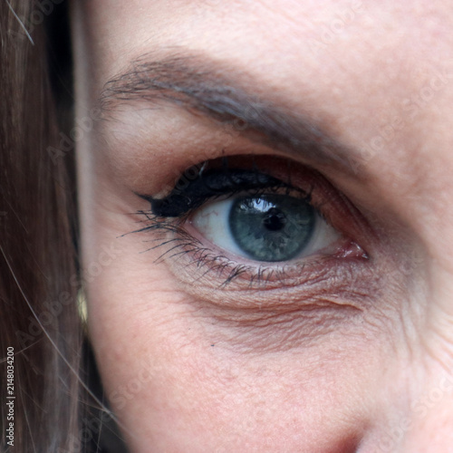 Dettaglio ravvicinato in primo piano di un occhio azzurro femminile con trucco eyeliner nero e rughe d'espressione sulla pelle matura