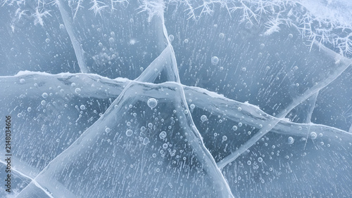 Intricate blue ice patterns feature frozen gas bubbles and deep structural cracks under bright winter sunlight