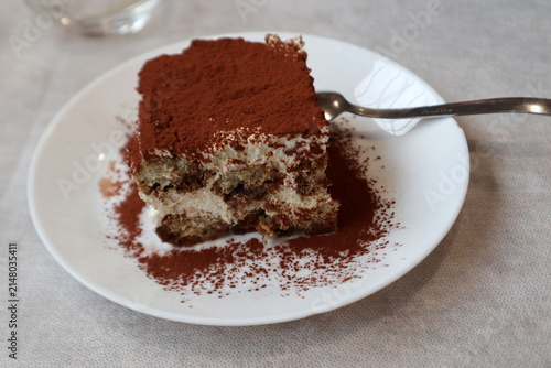 Porzione di tiramisù artigianale servita su un piatto bianco con polvere di cacao e un cucchiaino da dessert sul tavolo di un ristorante