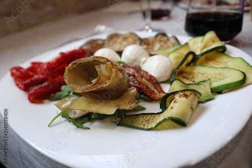 Piatto ricco di antipasto all'italiana con verdure grigliate, zucchine a nastro, melanzane, carciofi sott'olio, pomodori secchi e ciliegine di mozzarella fresca