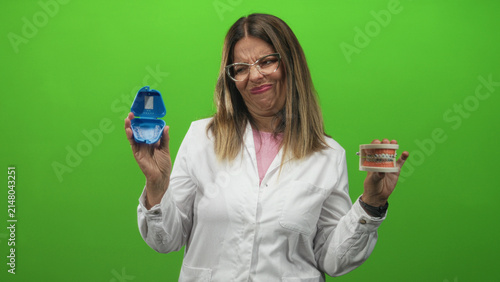 Canvastavla Woman dentist holding clear aligner case and dental model while grimacing and demonstrating aligner use in studio; skepticism