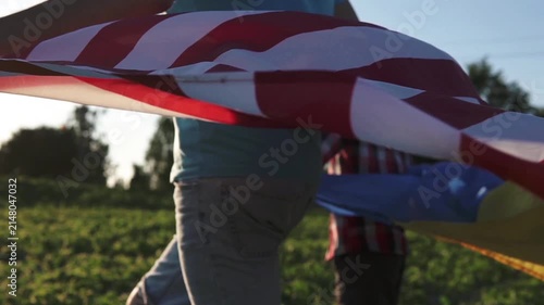 Back view of a father and son walking with Ukrainian and USA flags at sunset.