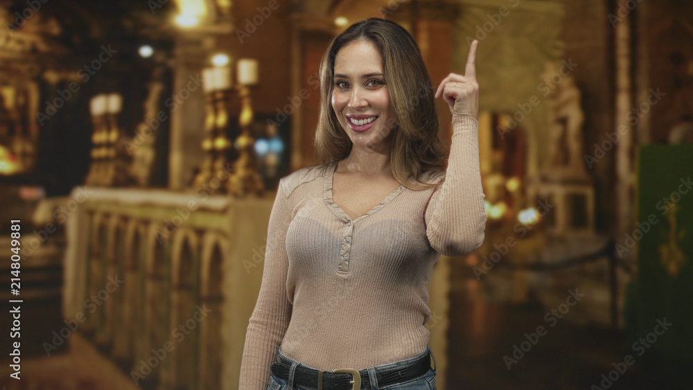 Obraz premium Woman pointing index finger upward at ornate altar inside building, wearing sweater and jeans, visible finger, thoughtful upward gaze; serenity.