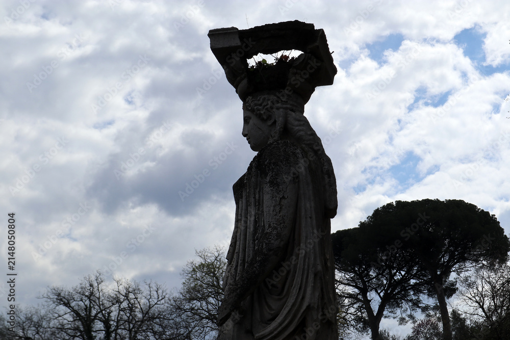 Fototapeta premium Statua classica di una Cariatide di profilo nell'area monumentale del Canopo di Villa Adriana sotto un cielo nuvoloso, Tivoli, Italia