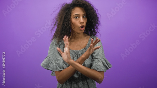 Quadro su tela Curly haired woman with crossed hands signaling stop and bare hands visible in a purple studio; rejection refusal boundary