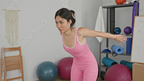 Konstfotografi Woman stretching arms in studio wearing pink bodysuit and reaching forward in a yoga training pose; focus calm balance