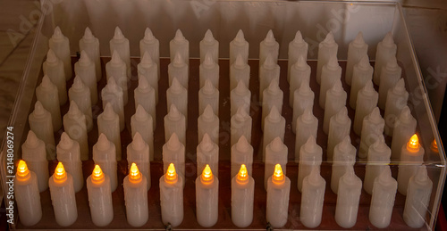 Canvastavla Rows of electronic prayer candles in a church with glowing yellow lights during