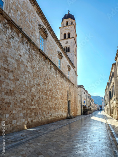 Historic limestone Stradun street in Dubrovnik featuring medieval stone architecture and tourists walking under clear sky.