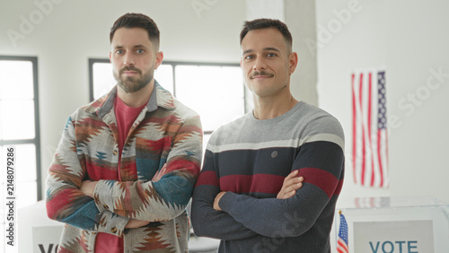 Foto Two men with arms crossed stand by a clear ballot box and american flag in a building; civic duty pride