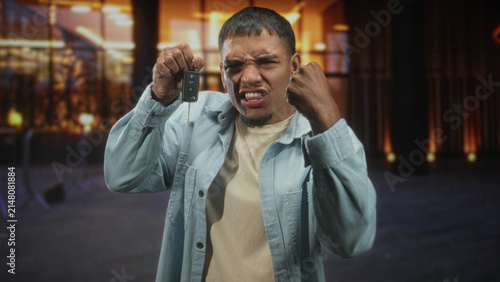 Принти на полотні Man holding car keys and clenched fist near face at a dimly lit building entrance; anger defiance tension