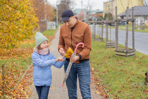 Child shares leaves with father on a tree-lined path covered in yellow leaves