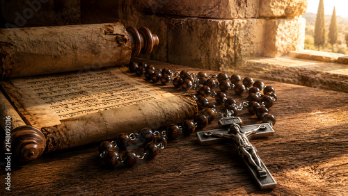 Antique wooden rosary with a silver crucifix lying next to an ancient parchment scroll on a rustic wooden table