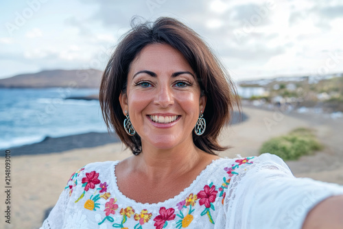 Smiling woman takes selfie at the beach with ocean background