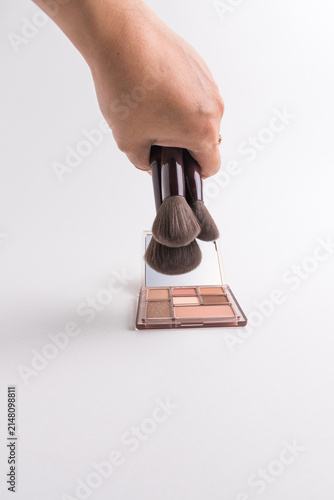 Canvastavla Hand holding bunch of makeup brushes over eyeshadow palette isolated on white ba