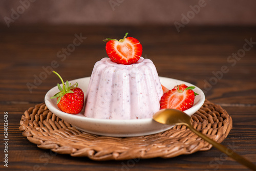 Homemade cottage cheese jelly dessert with chia seeds and fresh strawberries on a brown wooden table with spoon.