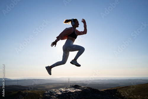 A white woman jumps energetically outdoors on a rocky hill in Galicia