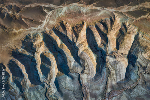 Aerial view of striped badlands ridges casting long shadows where erosion has carved fine drainage channels