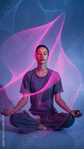 Woman meditating with colorful light trails and digital effects around her.