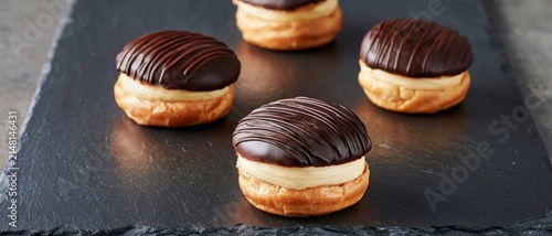Four delicious chocolate eclairs filled with cream on a dark slate surface