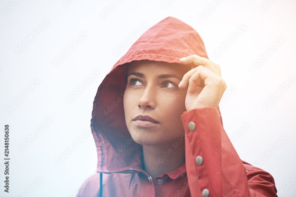 Fototapeta premium Woman, rain jacket and thinking with hood for weather, cloudy sky or winter season in outdoor storm. Face of female person with red waterproof coat in wonder for rainy overcast or fog on mockup space