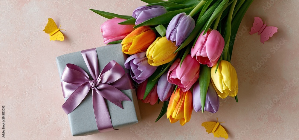 Obraz premium A vertical design featuring colorful tulips, an elegantly wrapped gift, silk bow, and paper butterflies on a soft pastel background.