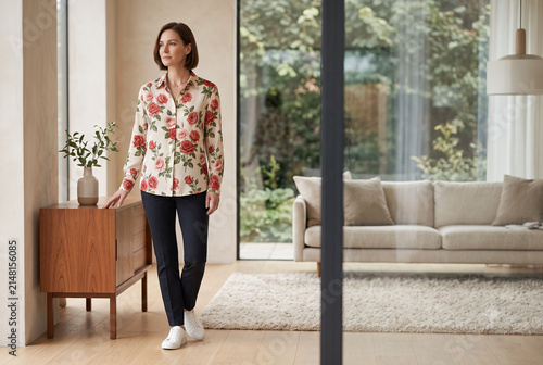 Elegant woman wearing rose print blouse in a bright modern living room with copy space