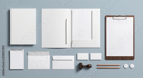 Top-down view of a white stationery branding mockup set with notebook, folder, business cards, and clipboard on a muted blue surface.