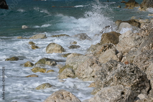 Rocky coast of Lefkada island with sea waves crashing on stones. Beautiful Mediterranean wild rocky beach background, Greece.