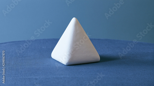 equilateral. Single white equilateral triangle object on deep blue linen, calm still life for editorial concept, lifestyle magazines.