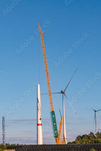 Heavy crawler crane assembling wind turbine tower under clear blue sky at wind farm, renewable green energy construction concept