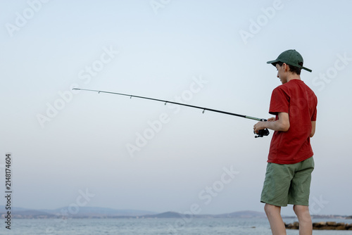 Teenager fish with rod by sea under cloudy sky