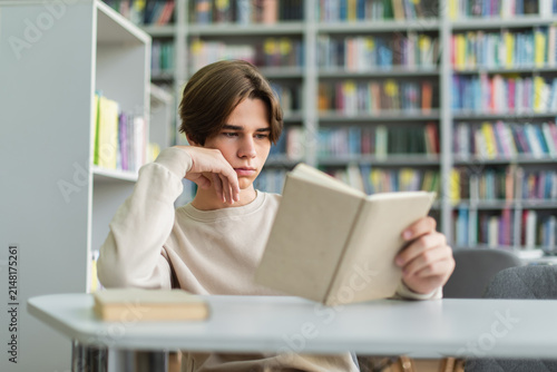 Принти на полотні Teenage boy absorbed in reading a book in a modern school library