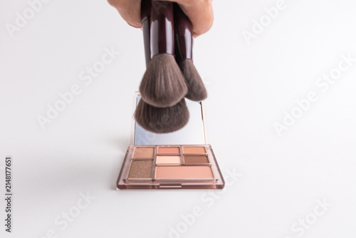 Photography Hand holding bunch of makeup brushes over eyeshadow palette isolated on white ba