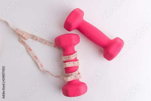 Pink dumbbells wrapped with measuring tape isolated on white background