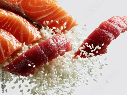 Fresh raw salmon and tuna slices with scattered sushi rice grains on white background, vibrant colors and high detail create appetizing and dynamic food composition