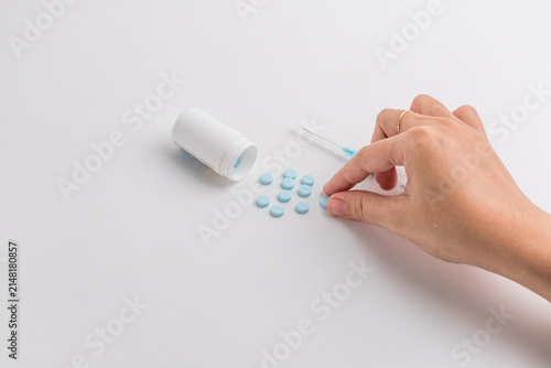 Light blue medical pills spilled from plastic bottle and syringe isolated on white background