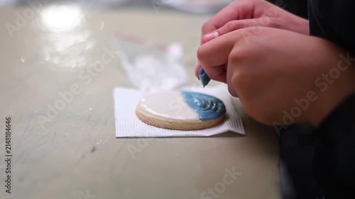 Professional pastry chef decorating cookie with blue royal icing and a toothpick for a custom design