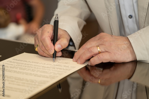 Fotografie Close-up of a person's hand signing an official document with a pen, wearing a g