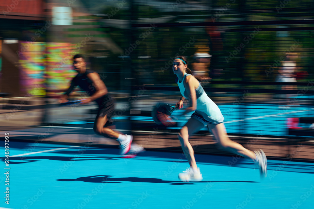 Obraz premium Stylish mixed padel pair running across court in coordinated sportswear with motion blur. Concept of couple activewear campaign, dynamic lifestyle fashion, sports partnership style.